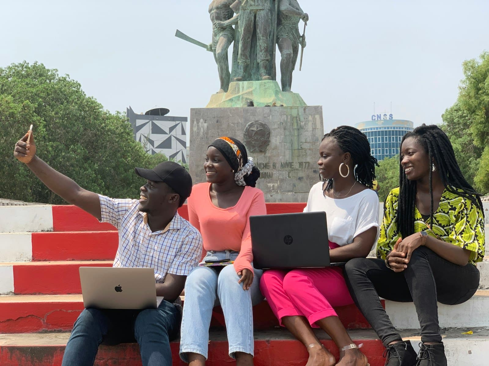 Four students sitting on red campus steps with their laptops